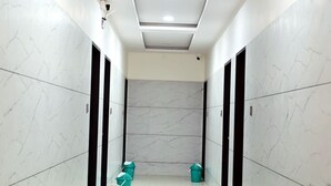 A hallway with white marble walls, black doors, and teal trash bins. - Hotel Paradise (Danta Ramgarh)