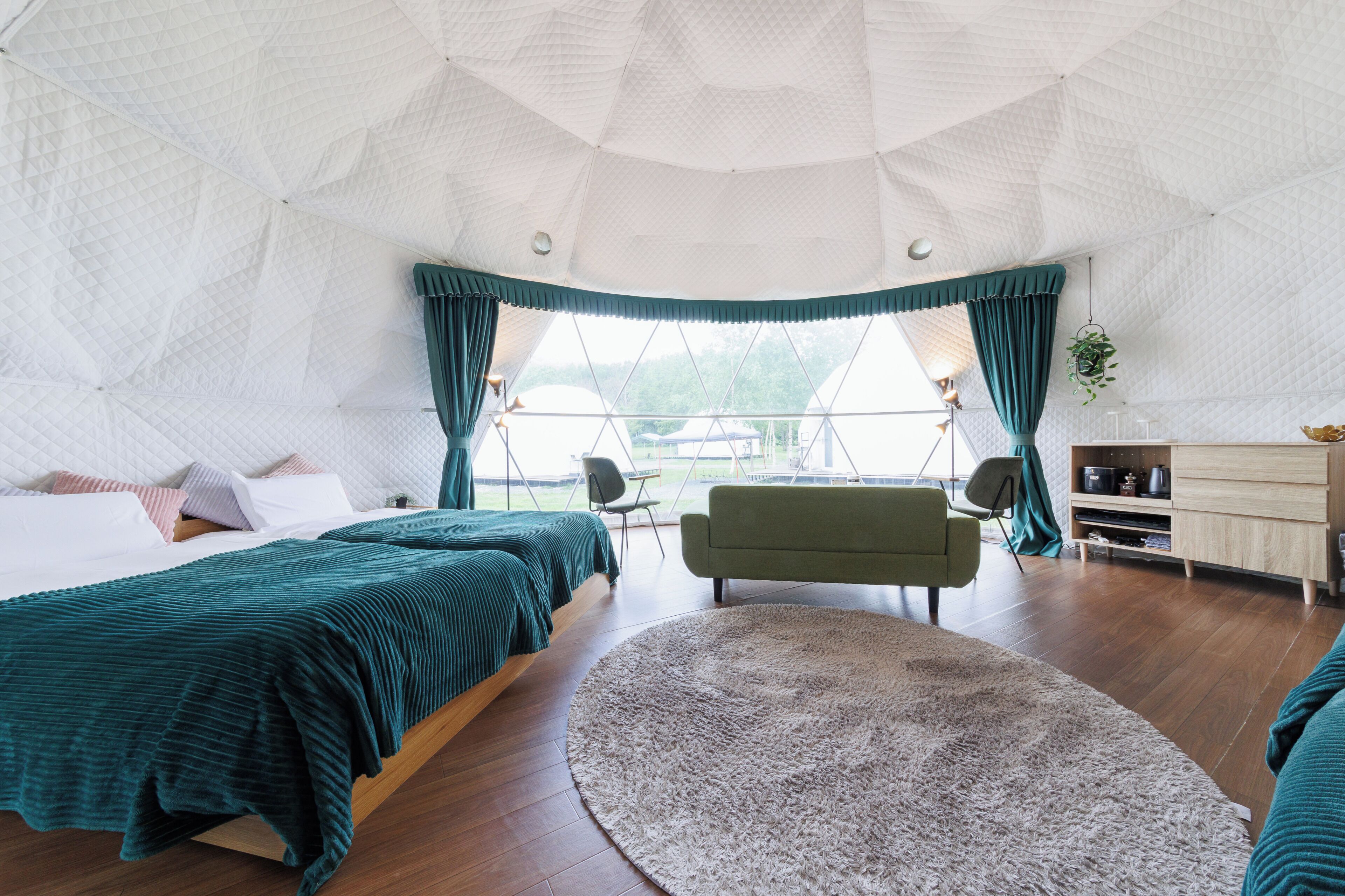 A spacious room with a large bed, a sofa, a round rug, and a view through a window.