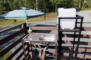 A portable outdoor kitchen setup with a sink, a table, and a chair, under a green canopy. - Gramping Stay Tomamu (Shimukappu)