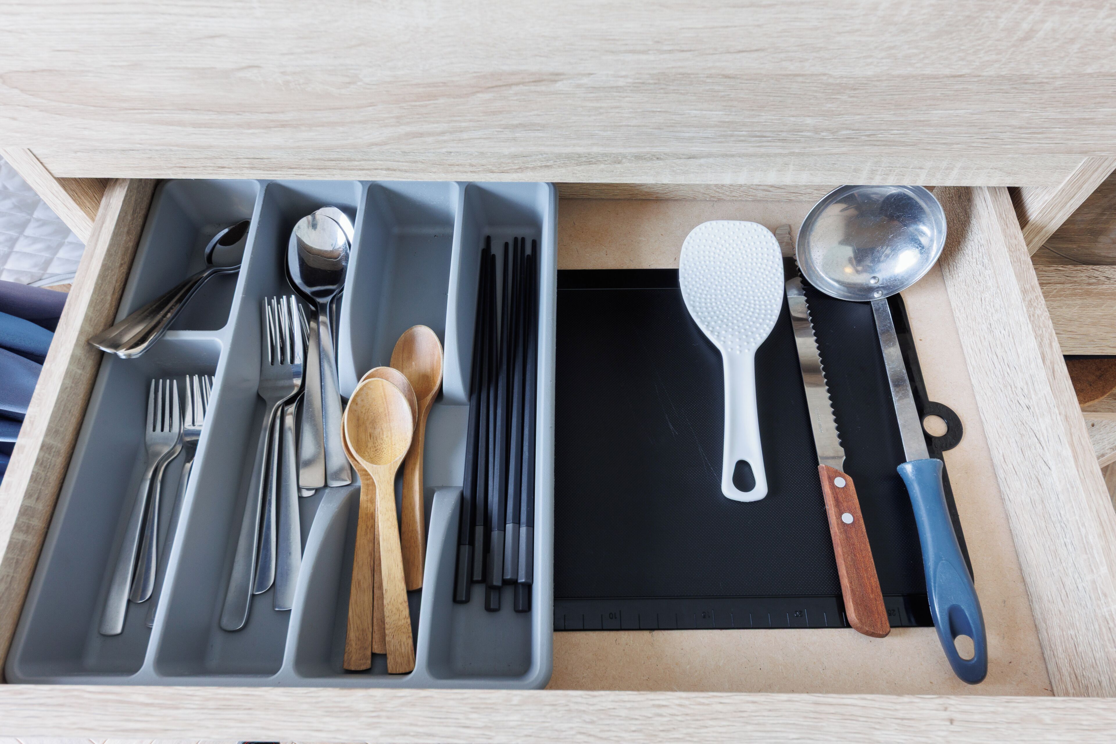 Un cajón con diversos utensilios de cocina, como cucharas, tenedores y una espátula.