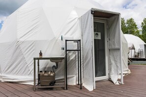 Una carpa blanca con una puerta, un lavamanos y un calentador portátil.