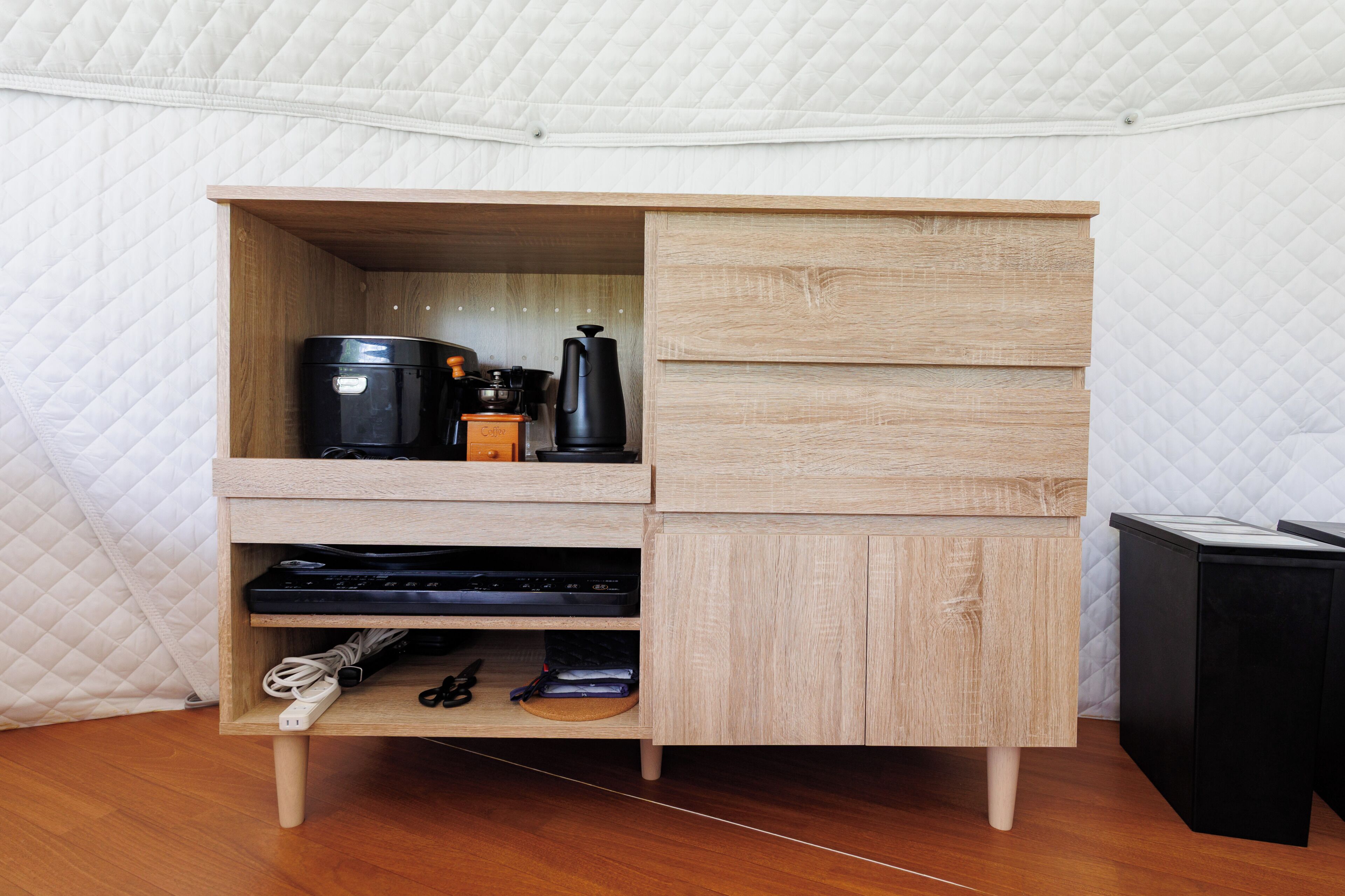 Ein kompakter Holzschrank mit integrierter Kaffeemaschine, Wasserkocher und einer kleinen Ablage für elektronische Geräte.