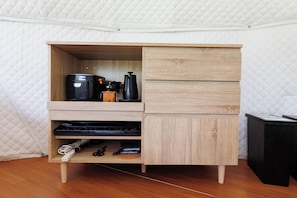 Un mueble de madera compacto con cafetera integrada, hervidor y un pequeño estante con dispositivos electrónicos.