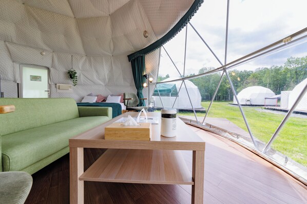 A tented accommodation with a wooden table, green sofa, and a view of the surrounding landscape. - Gramping Stay Tomamu (Shimukappu)