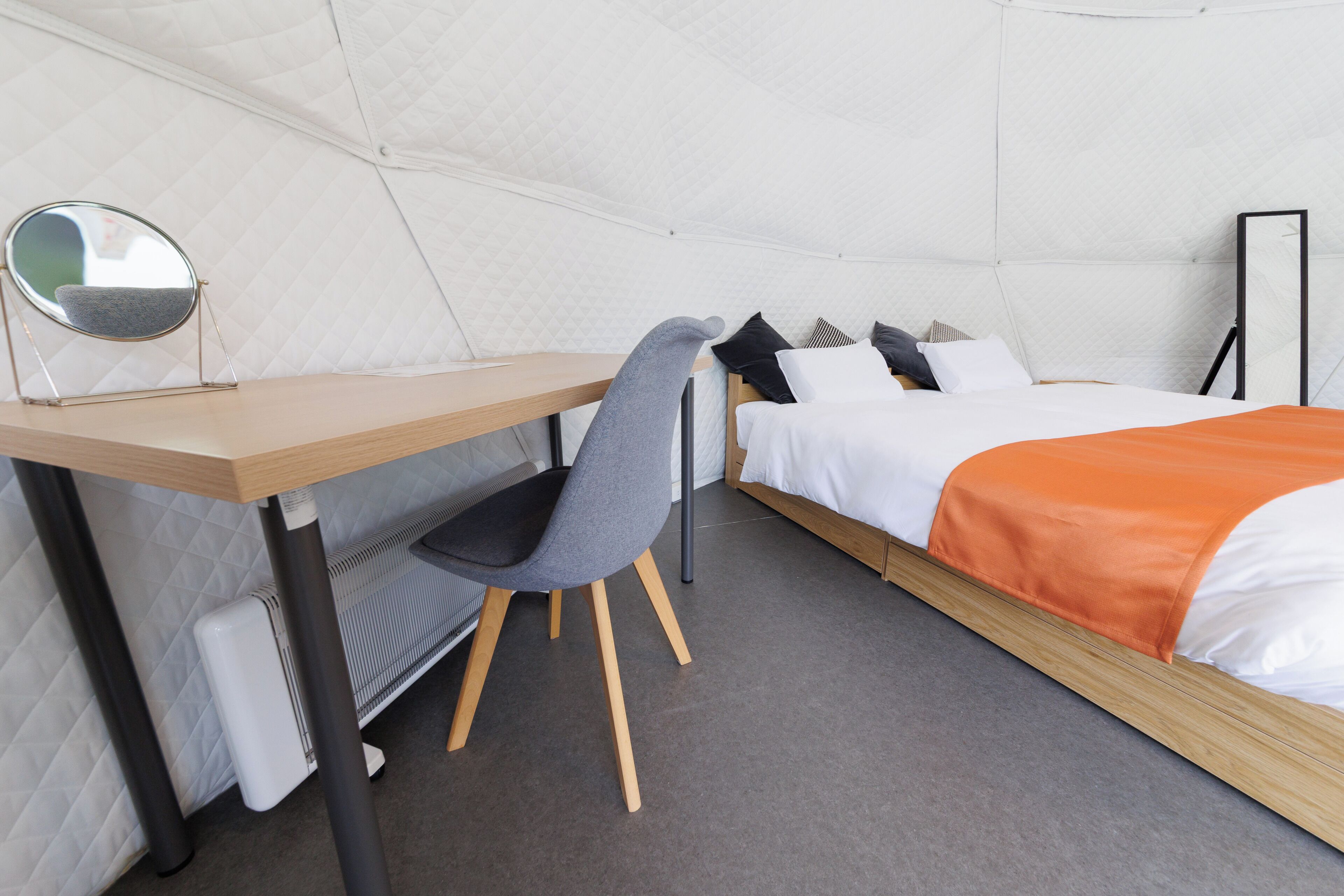 A compact room with a bed, a desk, a chair, a mirror, and a radiator.