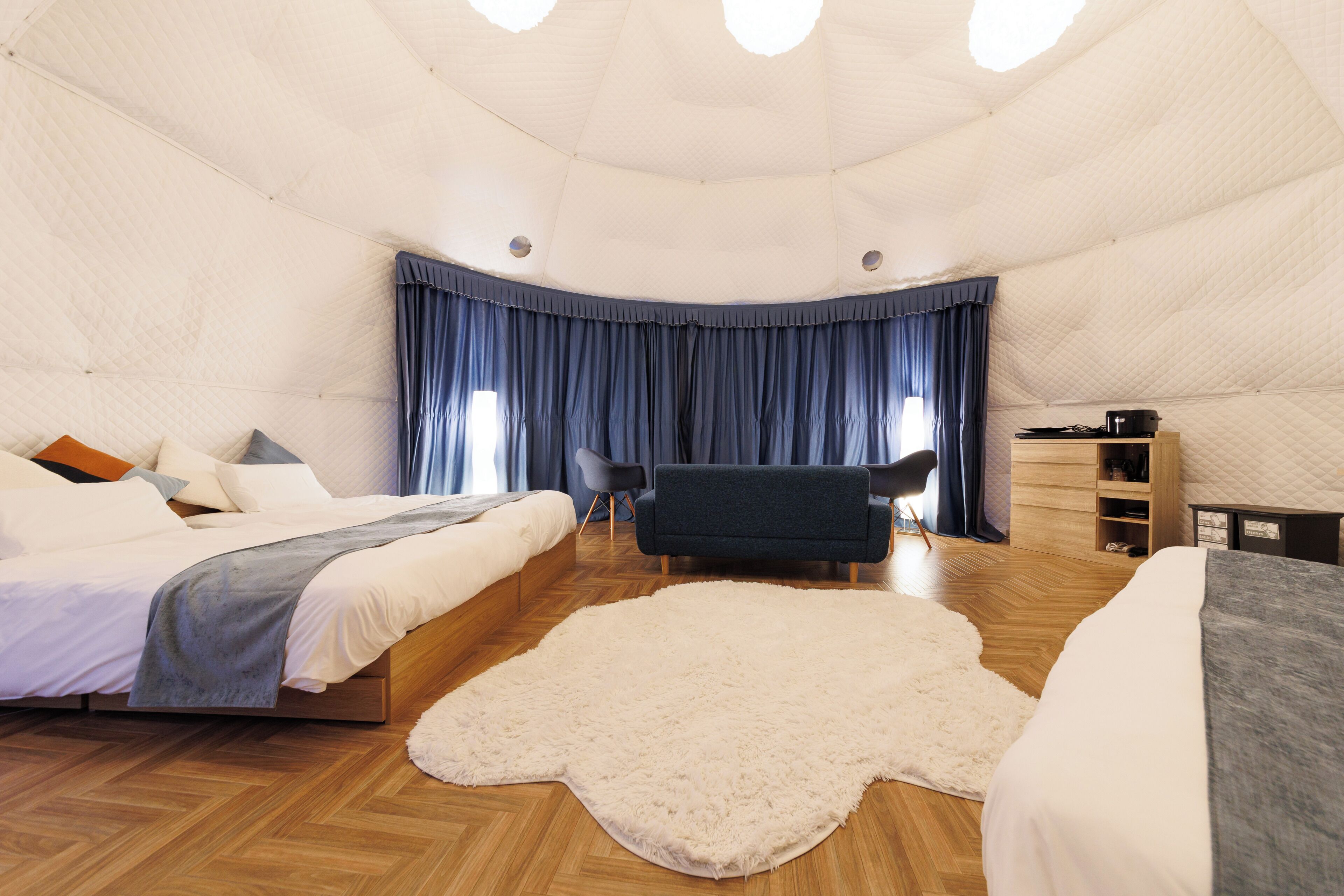 Ein zeltartiges Zimmer mit einem Bett, einem Sessel, einem Holzschrank und einem Fellteppich.