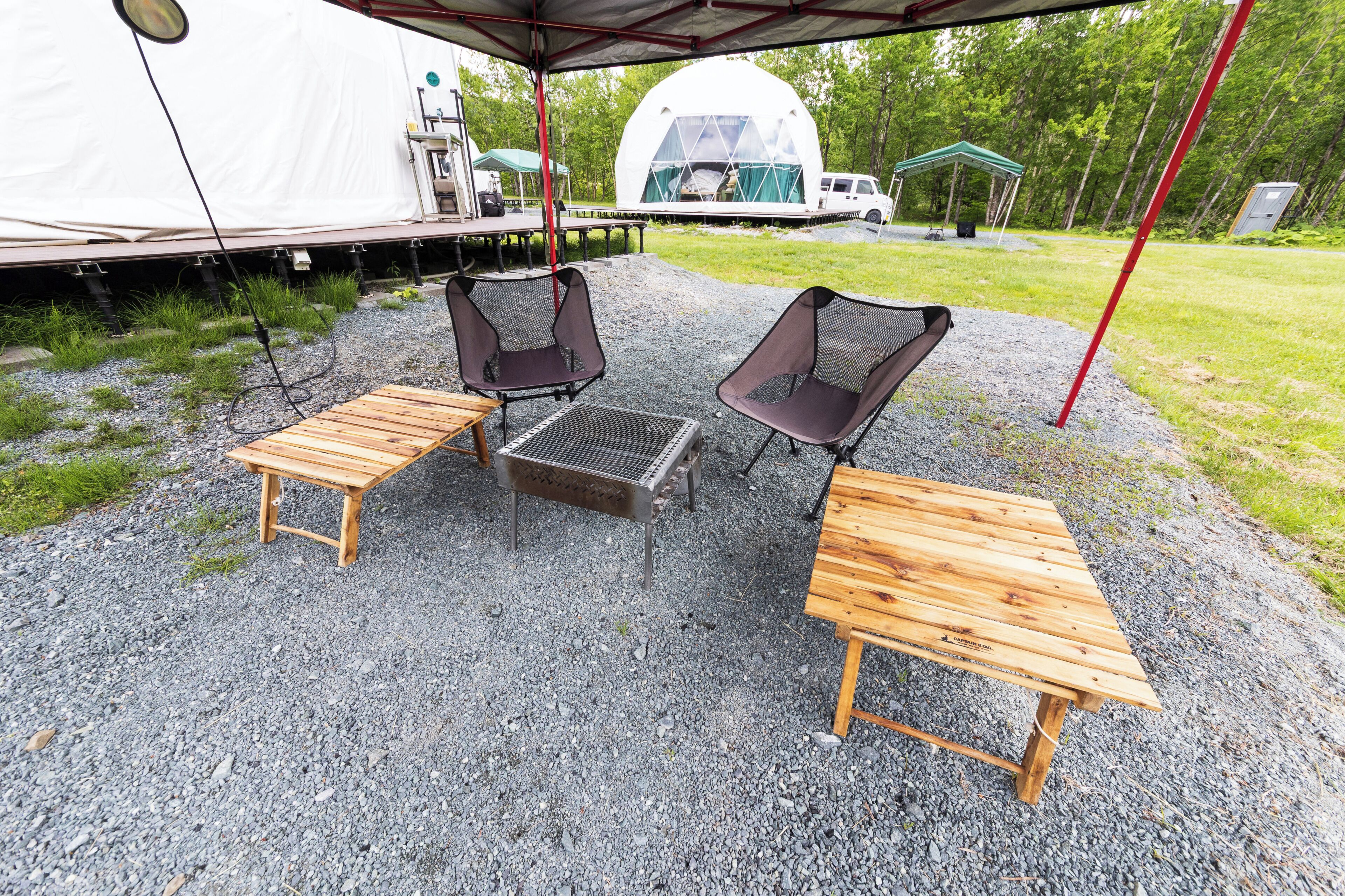 A campsite with a tent, two wooden tables, and two chairs.