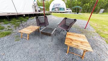 A campsite with a tent, two wooden tables, and two chairs.