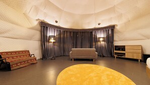 A room with a round yellow rug, a sofa, a TV stand, and curtains. - Gramping Stay Tomamu (Shimukappu)