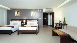 Ein Hotelzimmer mit zwei Einzelbetten, einem Schlafsofa, einem kleinen Tisch und einem Schreibtisch mit Stuhl.