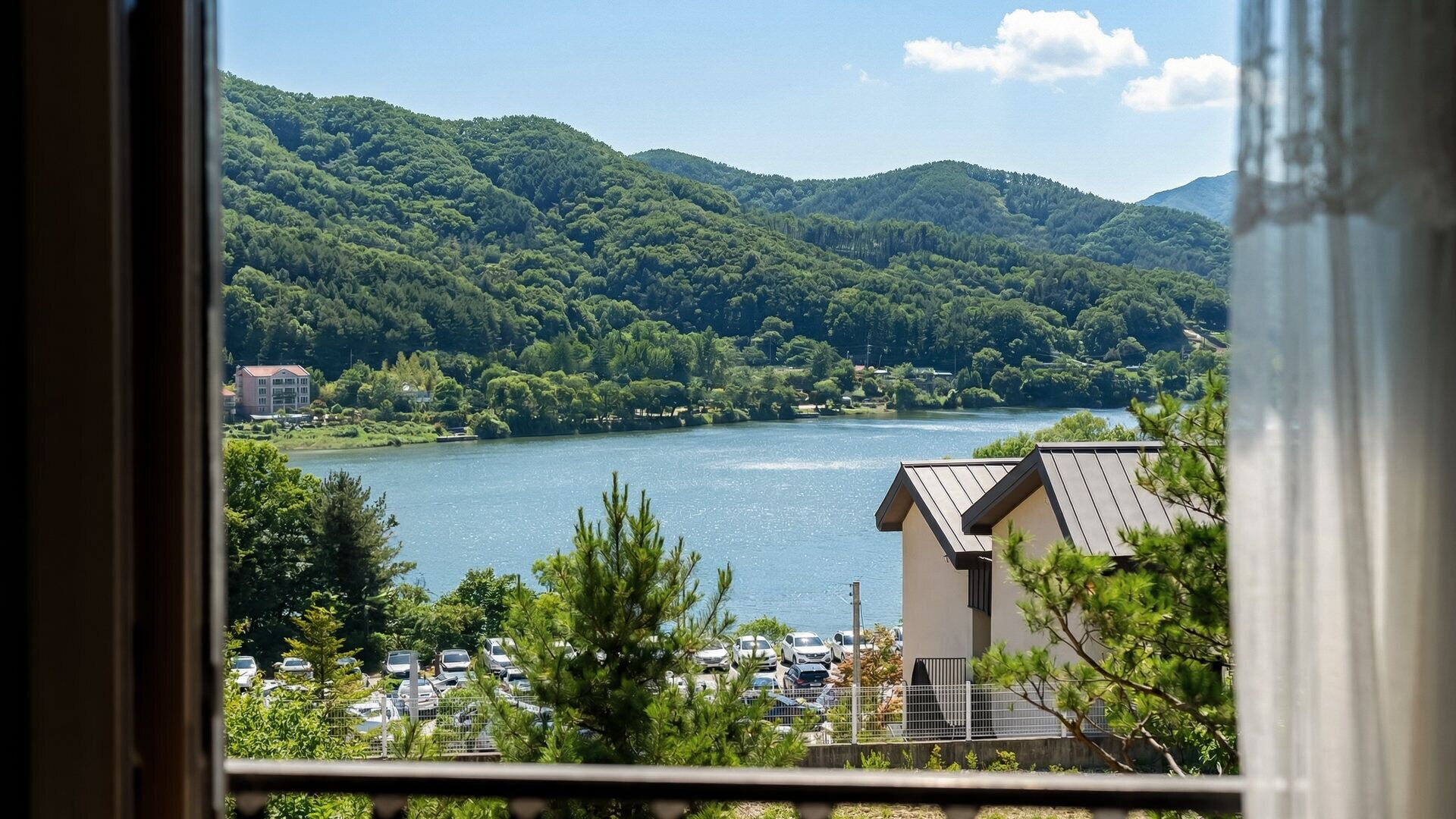 A lake with surrounding hills, a parking lot, and a building with a sloped roof.