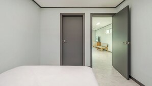 A bedroom with a bed, a closed door, and an open door leading to a hallway with a bench and a television. - Migasil Family & Private Pension (Gapyeong)