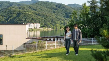 Una pareja caminando sobre un área verde con un lago y montañas al fondo.