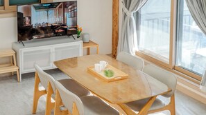 A dining area with a wooden table, two chairs, a tray with a plant, and a television on a cabinet. - Migasil Family & Private Pension (Gapyeong)