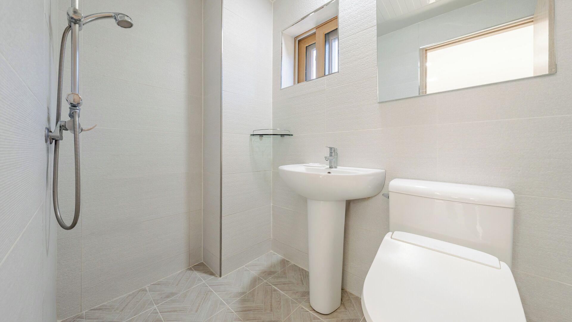 A bathroom with a shower, sink, toilet, and a window.