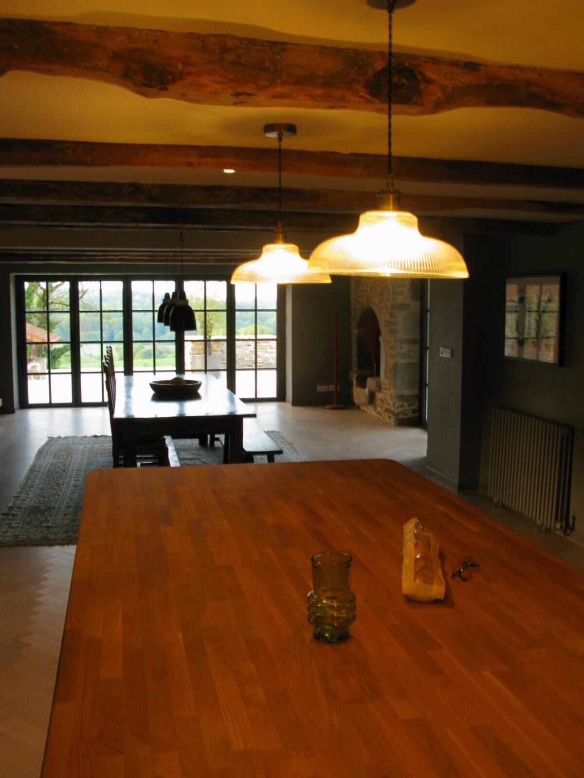 A spacious dining area with a large wooden table, pendant lighting, and a view through large windows to the outdoors.