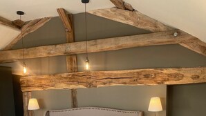 Ein Schlafzimmer mit einem großen Bett, Holzbalken, zwei Nachttischen mit Lampen und einem modernen Deckenscheinwerfer.