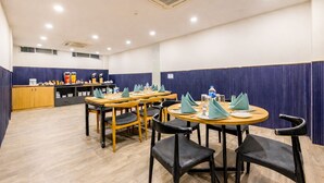 Un comedor de hotel con mesas redondas, sillas negras y cortinas azules.