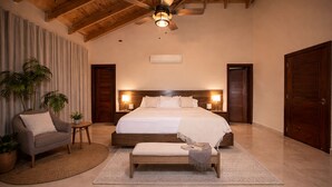 A bedroom with a large bed, wooden headboard, bedside lamps, a bench, and a ceiling fan. - Puerto Plata | Modern Villa Pool+BBQ+WiFi+Security (Puerto Plata)