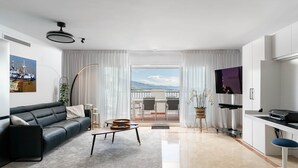 A modern living room with a black leather sofa, a coffee table, and a view of the outdoors through large windows. - Exclusive Penthouse in Paraíso Pueblo – Style & Serenity (Benahavís)