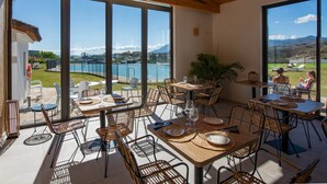 An outdoor dining area with tables and chairs, large windows, and a view of a lake and mountains. - Exclusive Penthouse in Paraíso Pueblo – Style & Serenity (Benahavís)