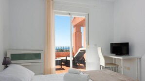 Una habitación de hotel con cama, televisión, escritorio y balcón con una silla y una mesa.