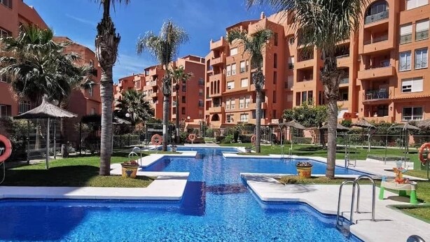 Un área de piscina con varias piscinas, palmeras y un edificio con balcones.