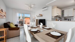 Una sala moderna con comedor, un sofá, televisor y una cocina con armarios y ventana.