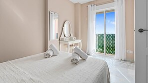 Une chambre avec un lit, un bureau, un miroir et un balcon offrant une vue.
