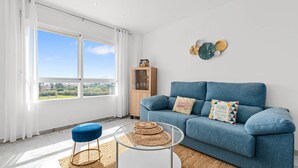 Un salon moderne avec un canapé bleu, une table basse en verre et une vue sur l’extérieur.
