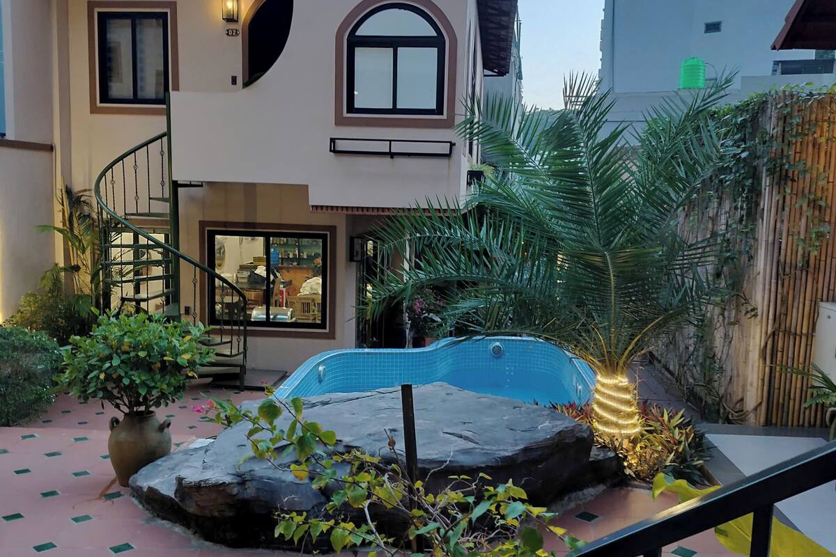 A two-story house with a swimming pool, a staircase, and a garden with plants and a rock feature.