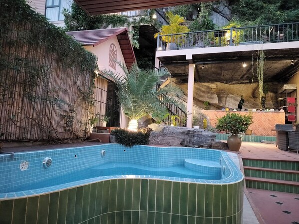 A swimming pool with a curved edge, surrounded by a bamboo fence and potted plants. - Secret Garden Homestay  (Cat Ba island)