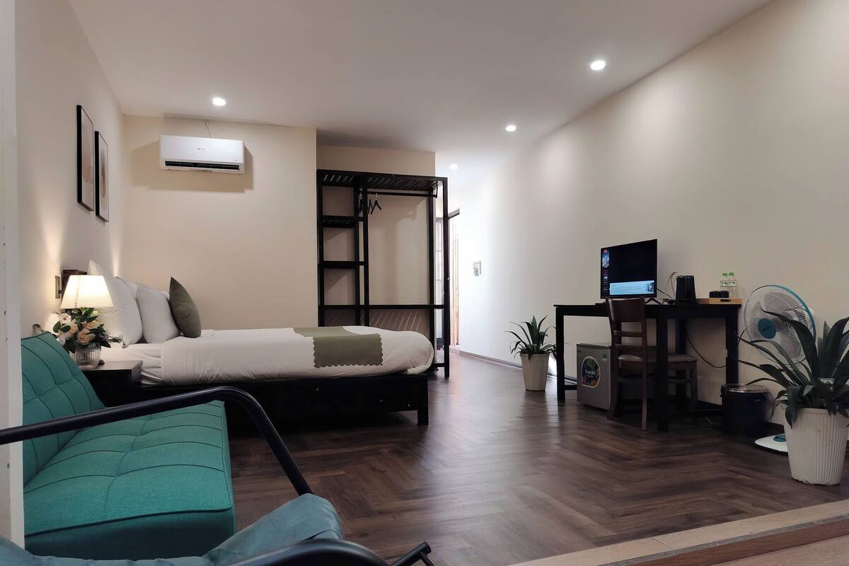 A modern bedroom with a bed, a desk with a computer, a chair, and a small table with a lamp.