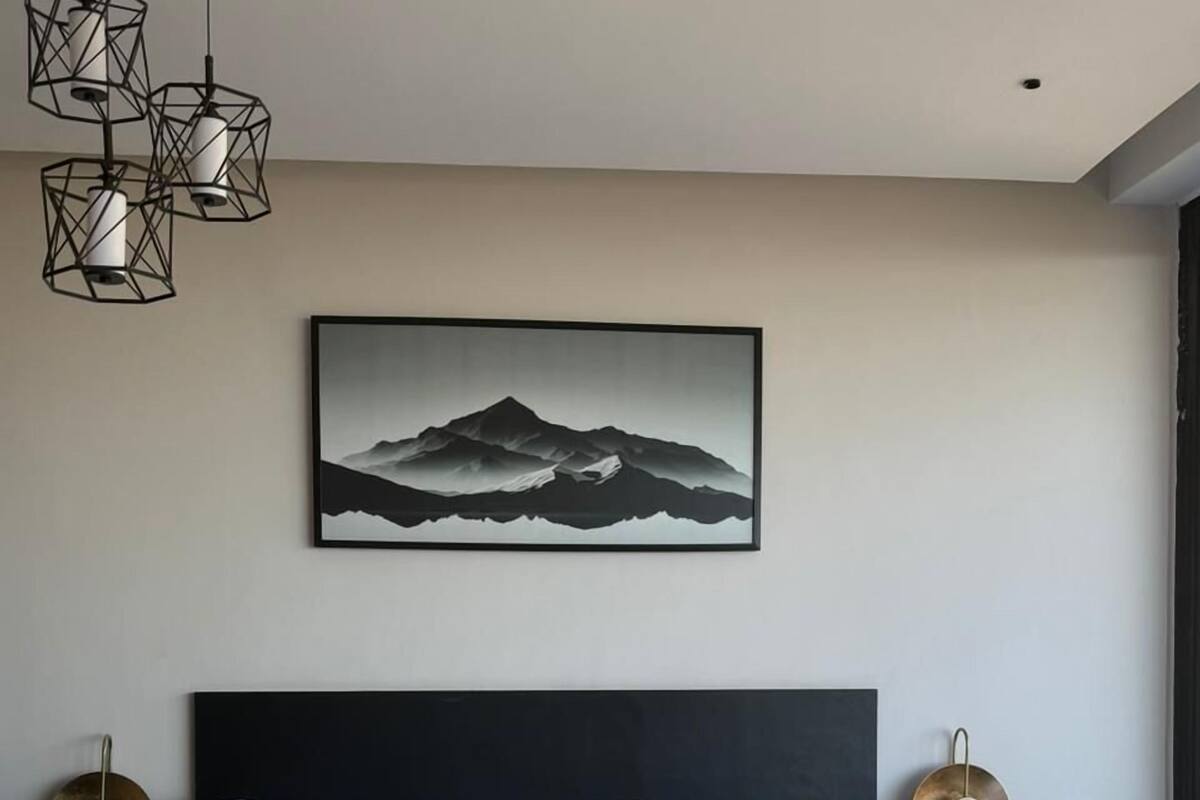 A modern bedroom with a large bed, a black headboard, and a mountain landscape painting on the wall.