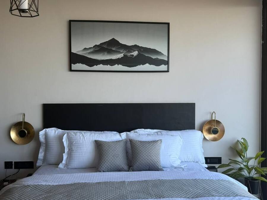 A modern bedroom with a large bed, a black headboard, and a mountain landscape painting on the wall.