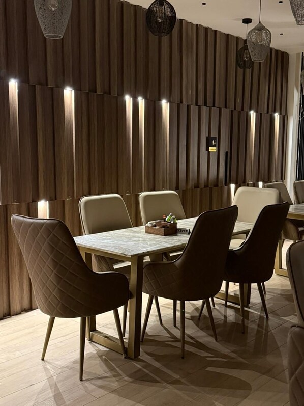 A modern dining area with a wooden panel wall, recessed lighting, and contemporary chairs. - Avatara (Dwarahat)