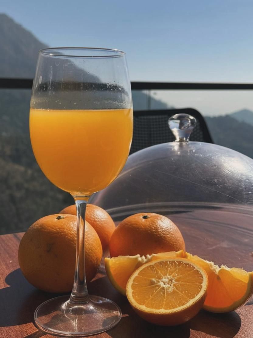 Um copo de suco de laranja, uma laranja inteira e meia laranja sobre uma mesa, com vista para montanhas ao fundo.
