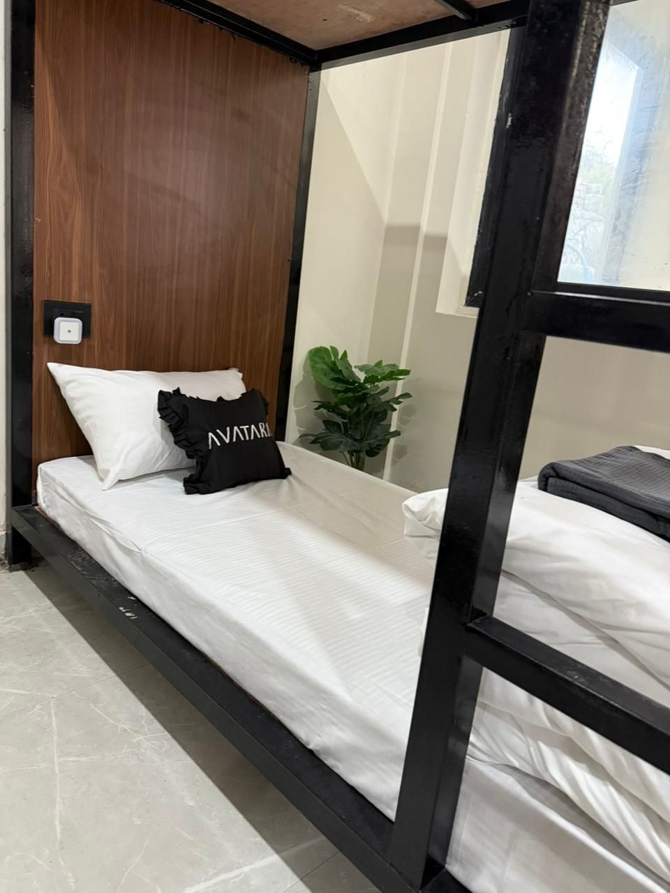 Una cama litera con cabecera de madera, una mesita de noche pequeña, una planta en maceta y un espejo.