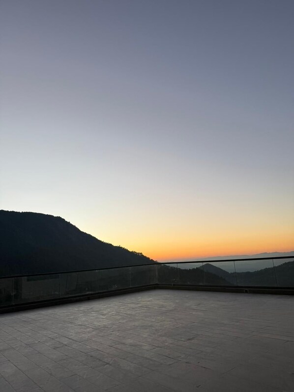 A spacious terrace with a clear view of a sunset over a hilly landscape.