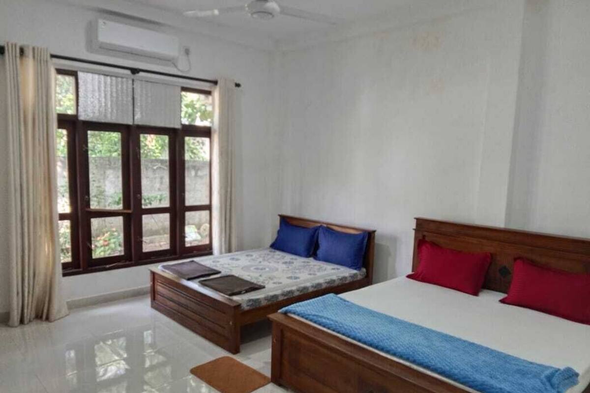 A bedroom with two beds, a window with curtains, and a ceiling fan.