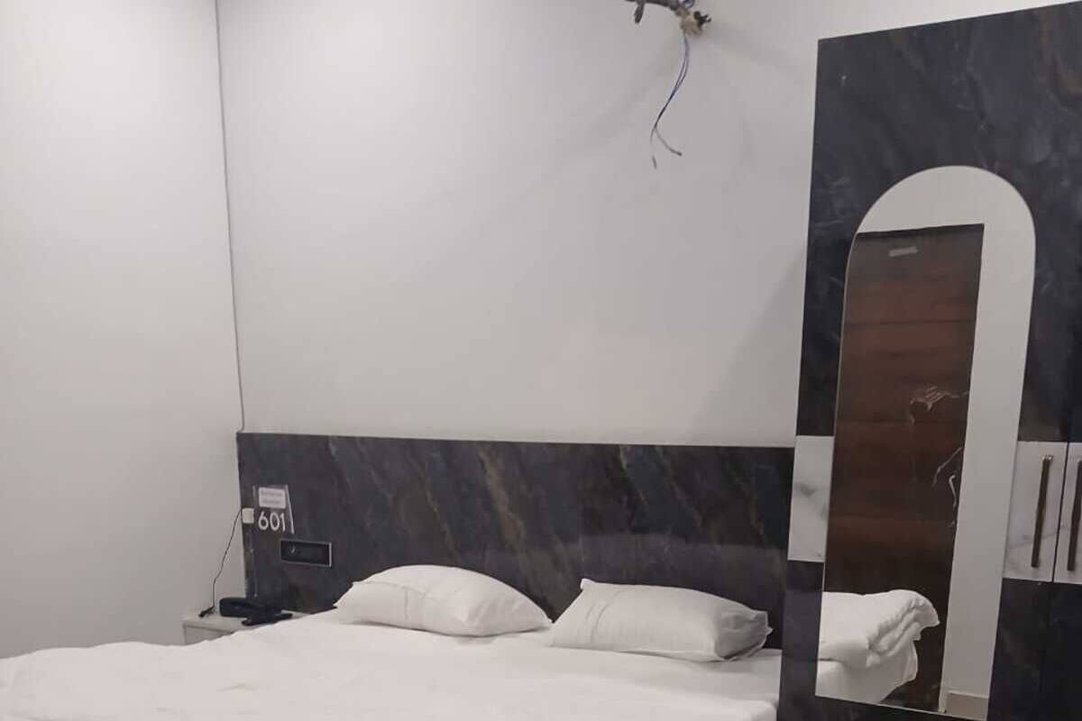 Une chambre moderne avec un grand lit, une table de chevet, un miroir fixé au mur et une tête de lit à motifs de marbre.
