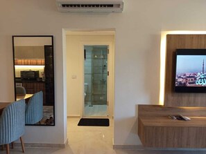 Ein modernes Wohnzimmer mit Fernseher, Holzschrank und Glastür zum Badezimmer.
