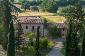 A stone building with a tiled roof, surrounded by trees and a grassy field. - Arco Apartment: Tuscan Charm and Relaxation (Colle di Val d'Elsa)