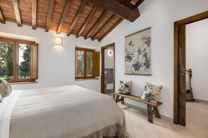 Une chambre à coucher avec un lit, un banc en bois, des œuvres d’art et une porte dotée d’un miroir.