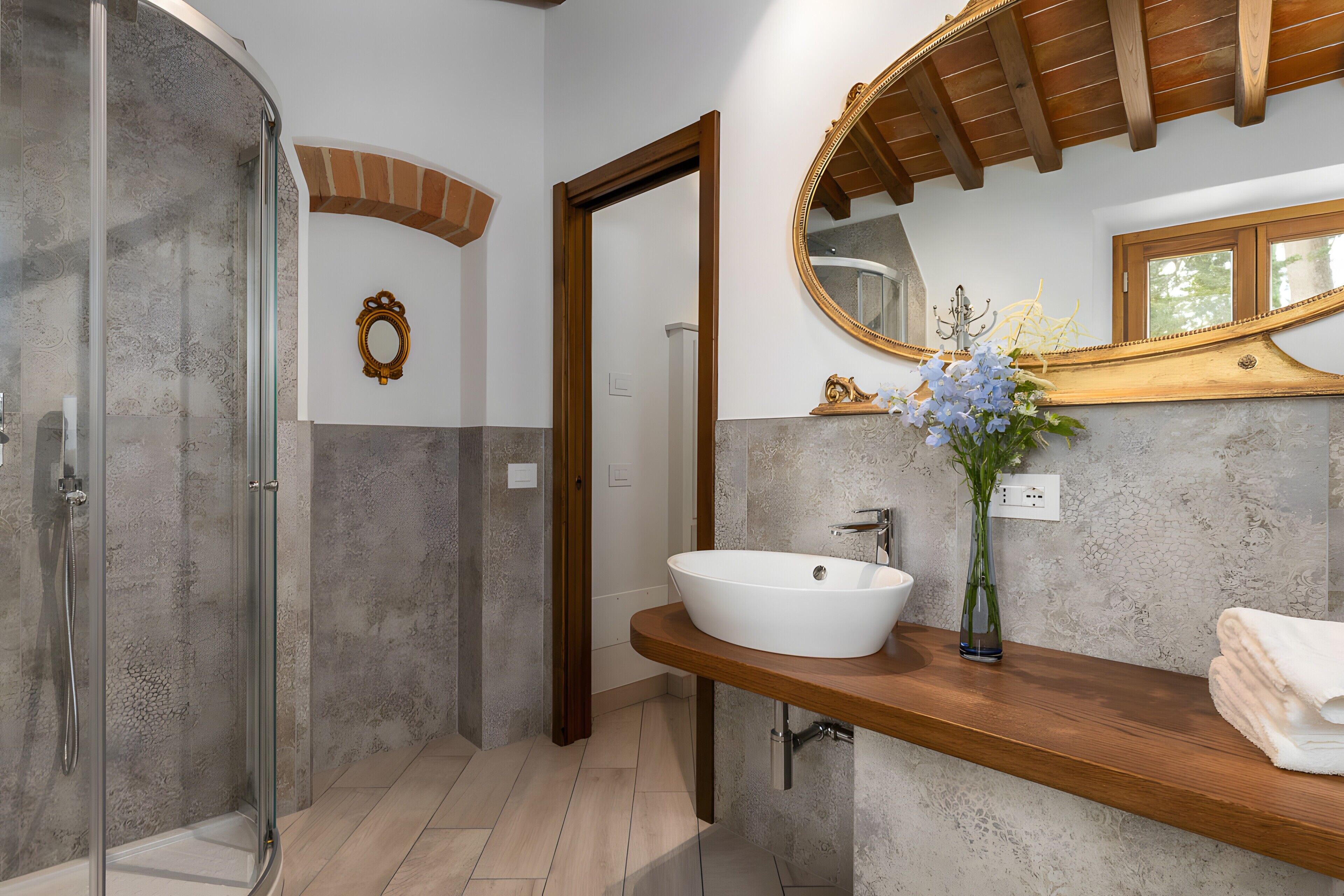 A bathroom with a glass shower enclosure, a white sink, a wooden vanity, and a large mirror.