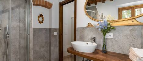A bathroom with a glass shower enclosure, a white sink, a wooden vanity, and a large mirror.