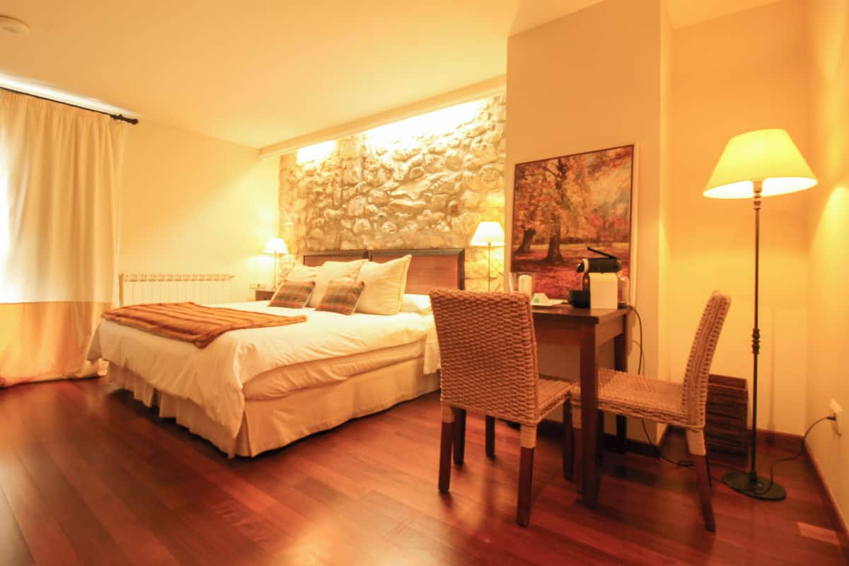 A bedroom with a bed, two chairs, a desk, a lamp, and a painting on the wall.
