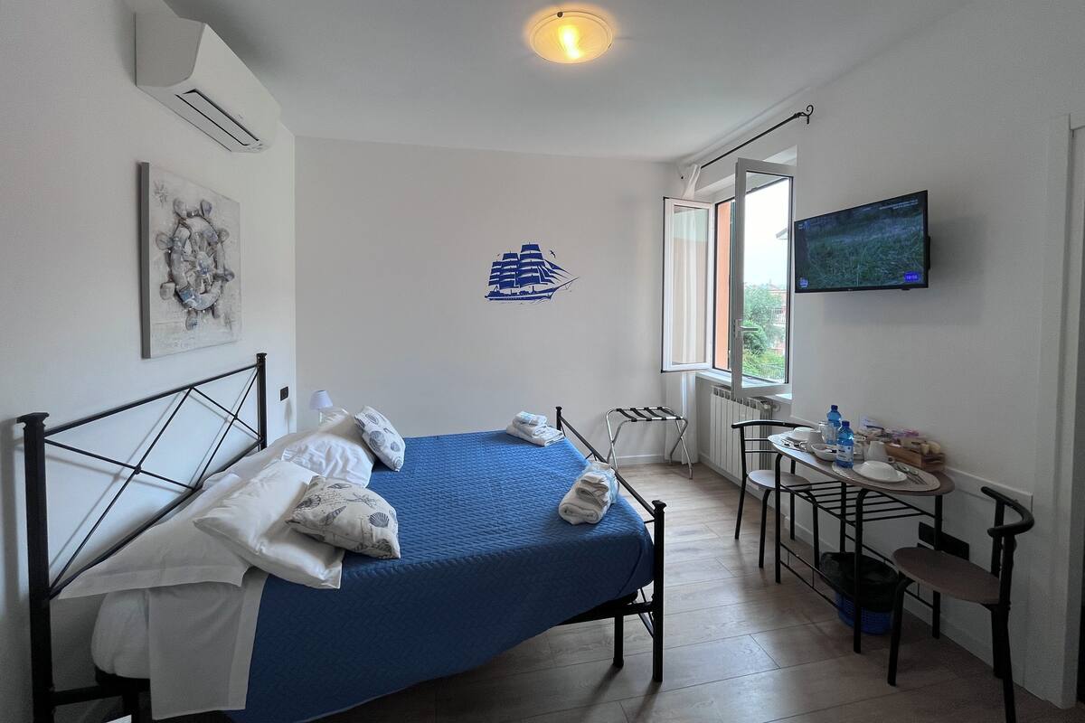 A neatly arranged bedroom with a bed, a small table with chairs, a TV, and a window with a view.