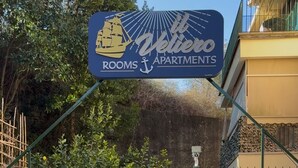 Une enseigne indiquant « Veliero Apartments », avec des places assises à l’extérieur et un portail vert.
