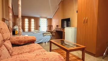 A compact room with a bed, a sofa, a small table, a TV, and a wardrobe.